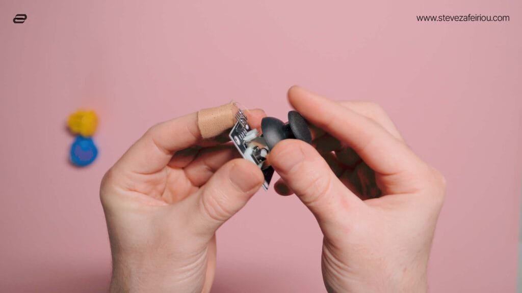 Hands demonstrating a small 2-axis joystick module, used in DIY arcade consoles and game controllers.