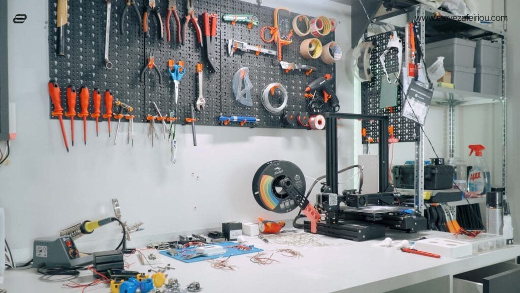 Organized DIY electronics workshop featuring various hand tools, a soldering station, 3D printer, filaments, and components essential for electronics and Arduino-based arcade gaming projects.