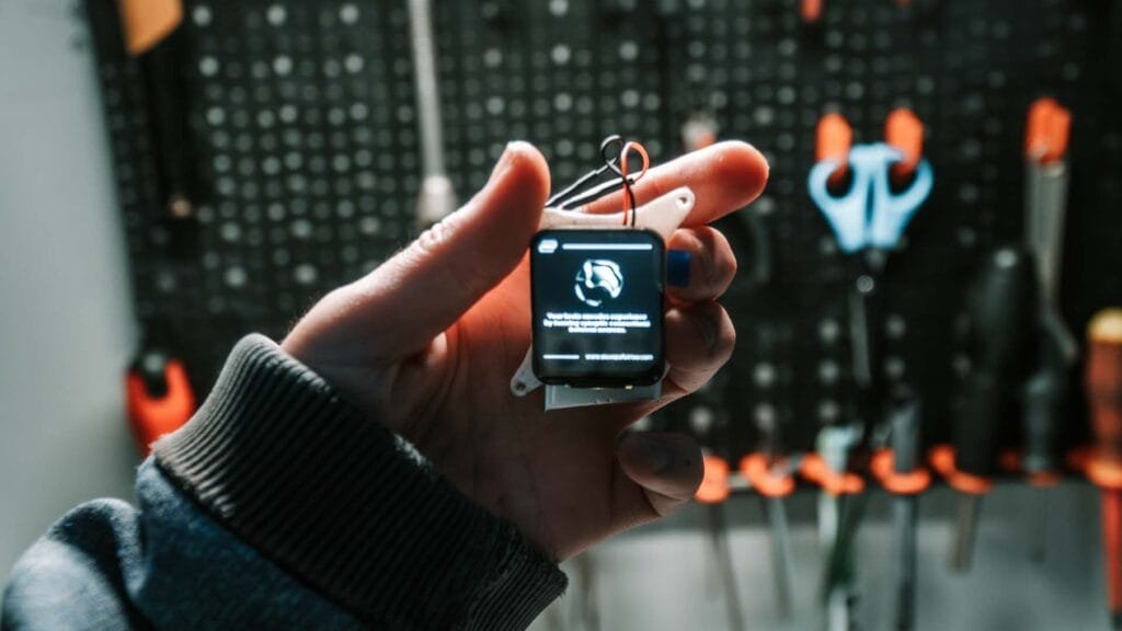Person holding Waveshare ESP32-S3 1.69 inch display module with custom digital artwork on screen in a workshop environment