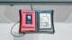 Close-up of a 'Synthetic Memories' interactive wearable device featuring a red and black 3D-printed casing with an embedded ESP32 screen and a nostalgic photo display.