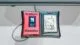 Close-up of a 'Synthetic Memories' interactive wearable device featuring a red and black 3D-printed casing with an embedded ESP32 screen and a nostalgic photo display.