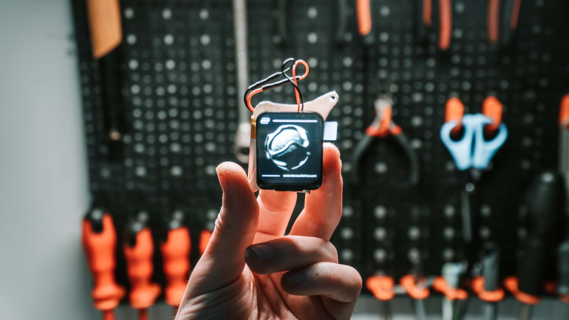 Close-up of ESP32-S3 1.69 inch display powered on, showing a graphics demo on TFT screen with visible wiring and tools in background