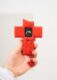 What Is a Microcontroller? Arduino & ESP32 Explained (2026) 25 Front view of an ESP32 handheld cross device (interactive art sculpture) in a person’s hand, red splatter-painted with screen, button, and keychain attachment.